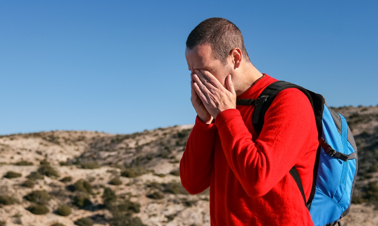 Picture of young man with his hands over his eyes. He has a migraine