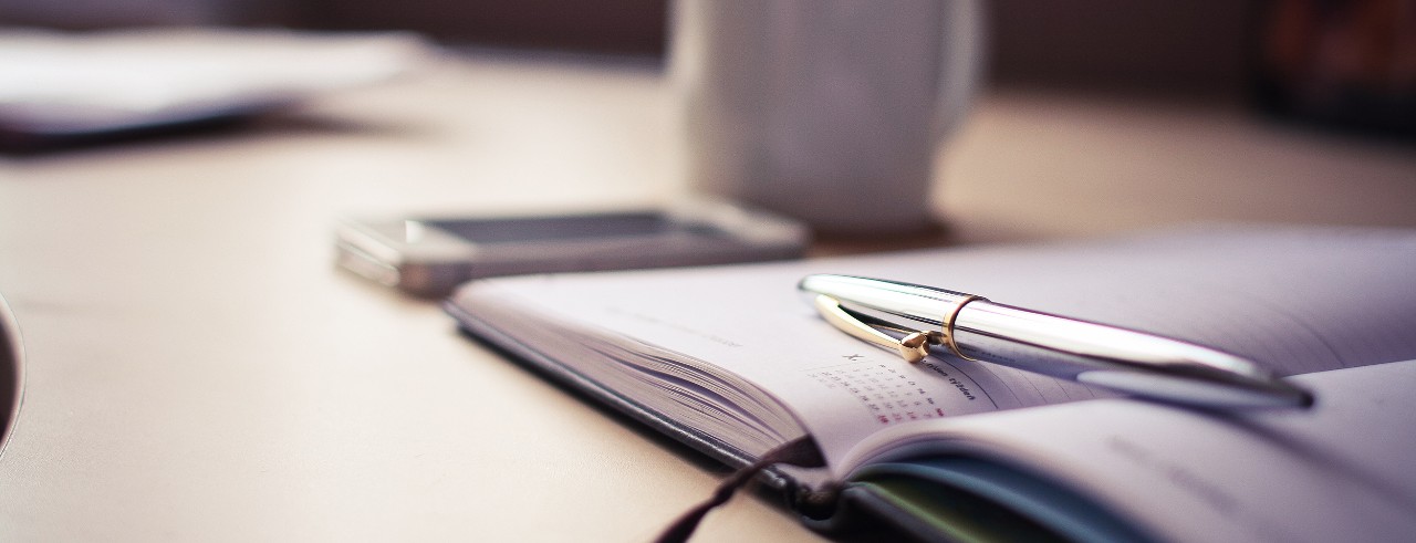 Book calendar, pen, smart phone and mug on a table.