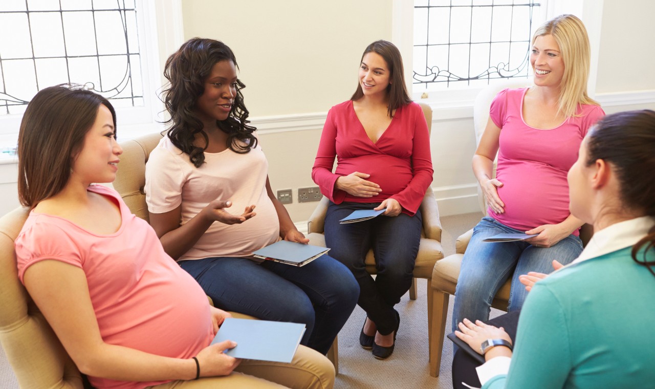 Five diverse pregnant women sit in a group with iPads.
