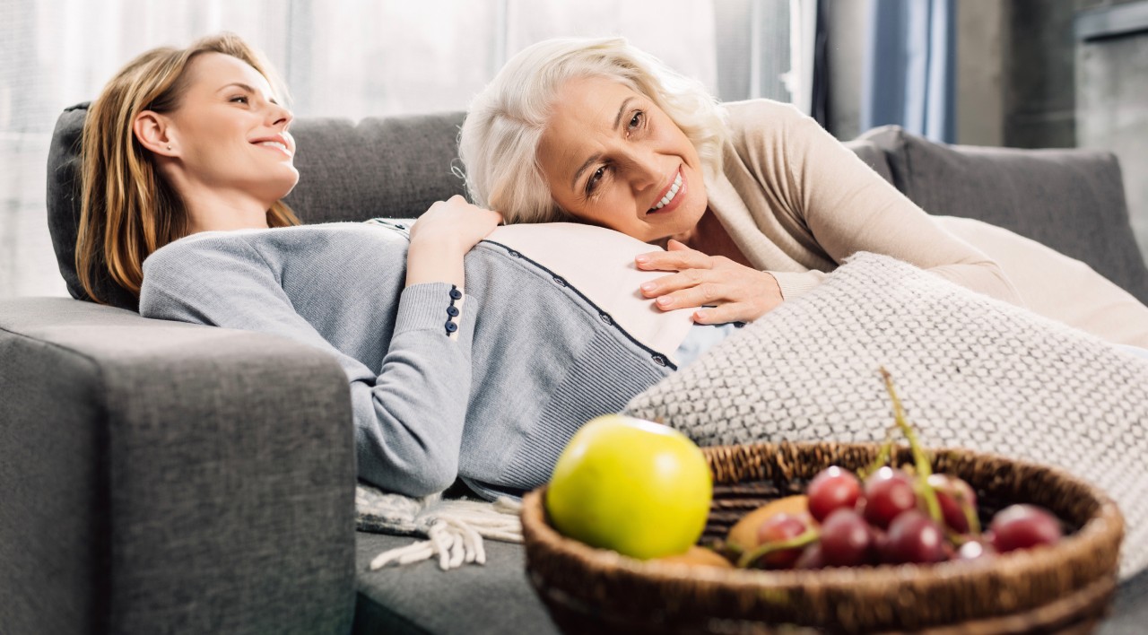 Mother leans on pregnant daughter's belly on a couch feeling the baby kick.