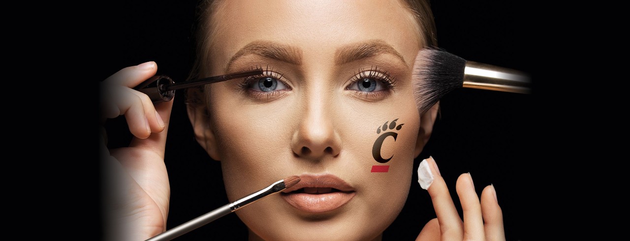 woman's face with UC bear paw tattoo and make-up brushes