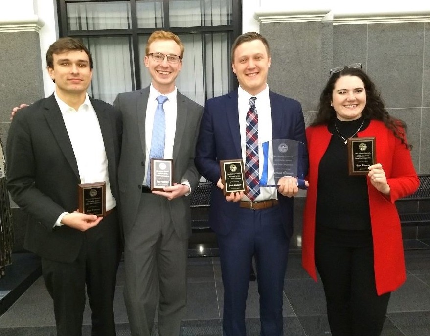 Four students smiling and holding plaques
