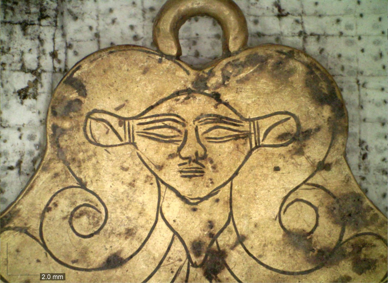 A gold pendant features the image of Hathor, an Egyptian goddess.