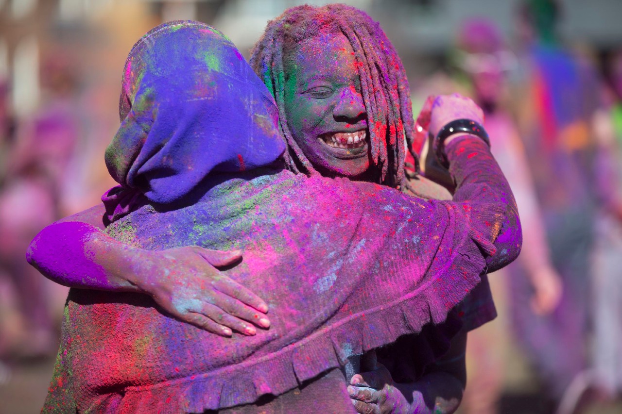 Two students hugging while covered in colored chalk during Holi celebration