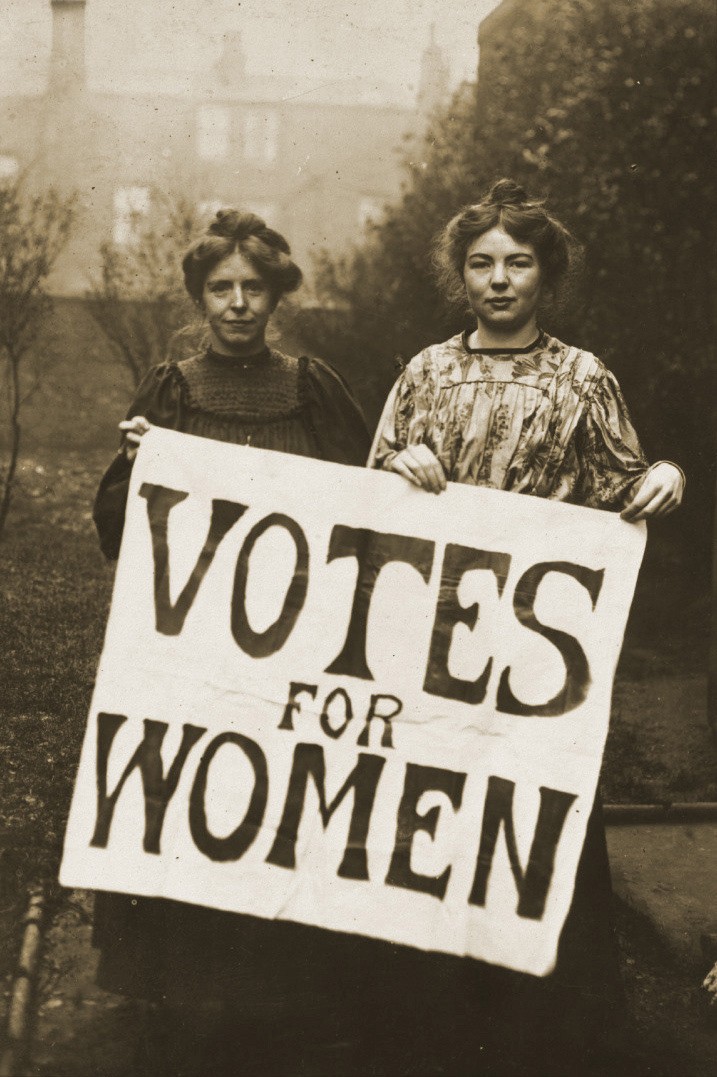 Old photo of two women suffrage activists holding "Votes for Women" sign.