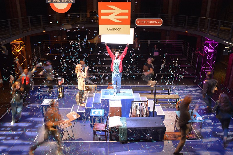 Actors on stage are covered in colorful confetti falling from the ceiling.