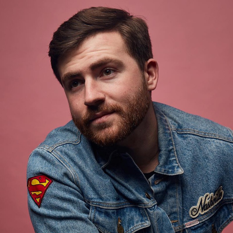 A headshot of Ryan Fine with a pink background
