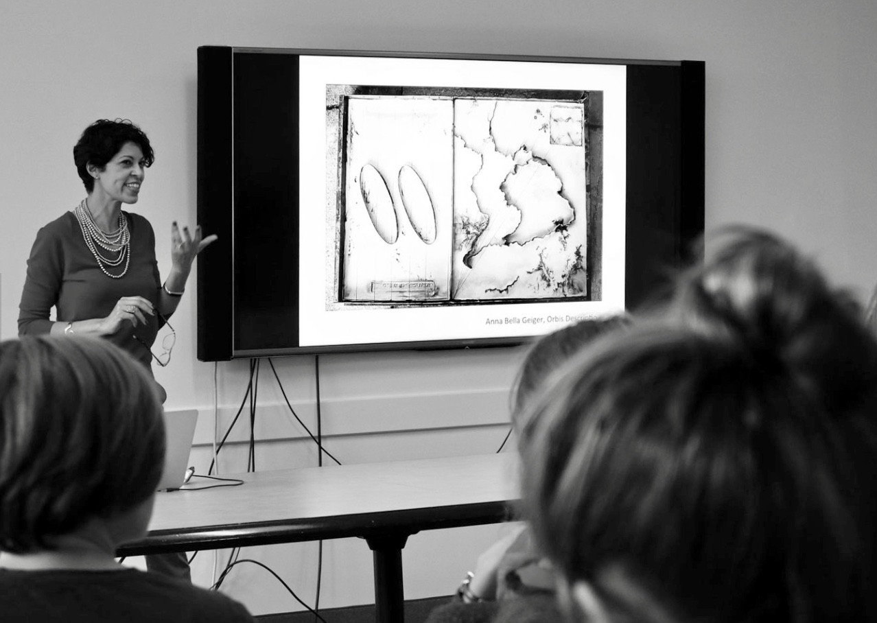 UC's Flavia Bastos stands in front of a large Powerpoint screen sharing her research with colleagues.