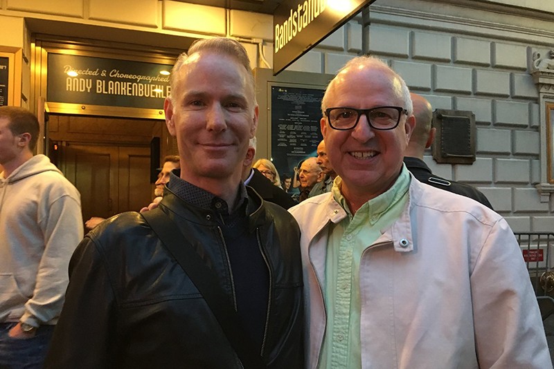 Two men smile under the lights of Broadway's "Bandstand" musical marquee. 