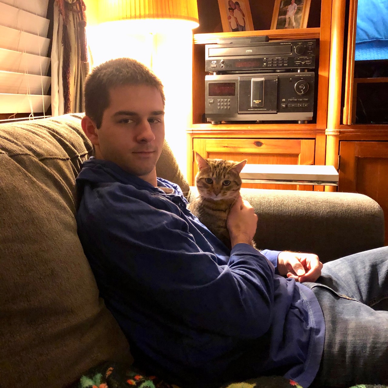 Man sits on couch holding a striped cat.