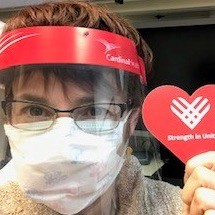Woman wearing face shield holding a red paper heart.