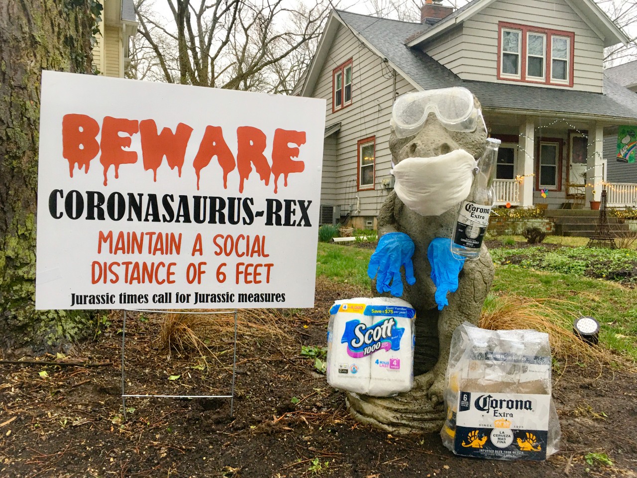 A cement T-Rex is dressed in goggles, gloves and a face mask surrounded by t-paper.