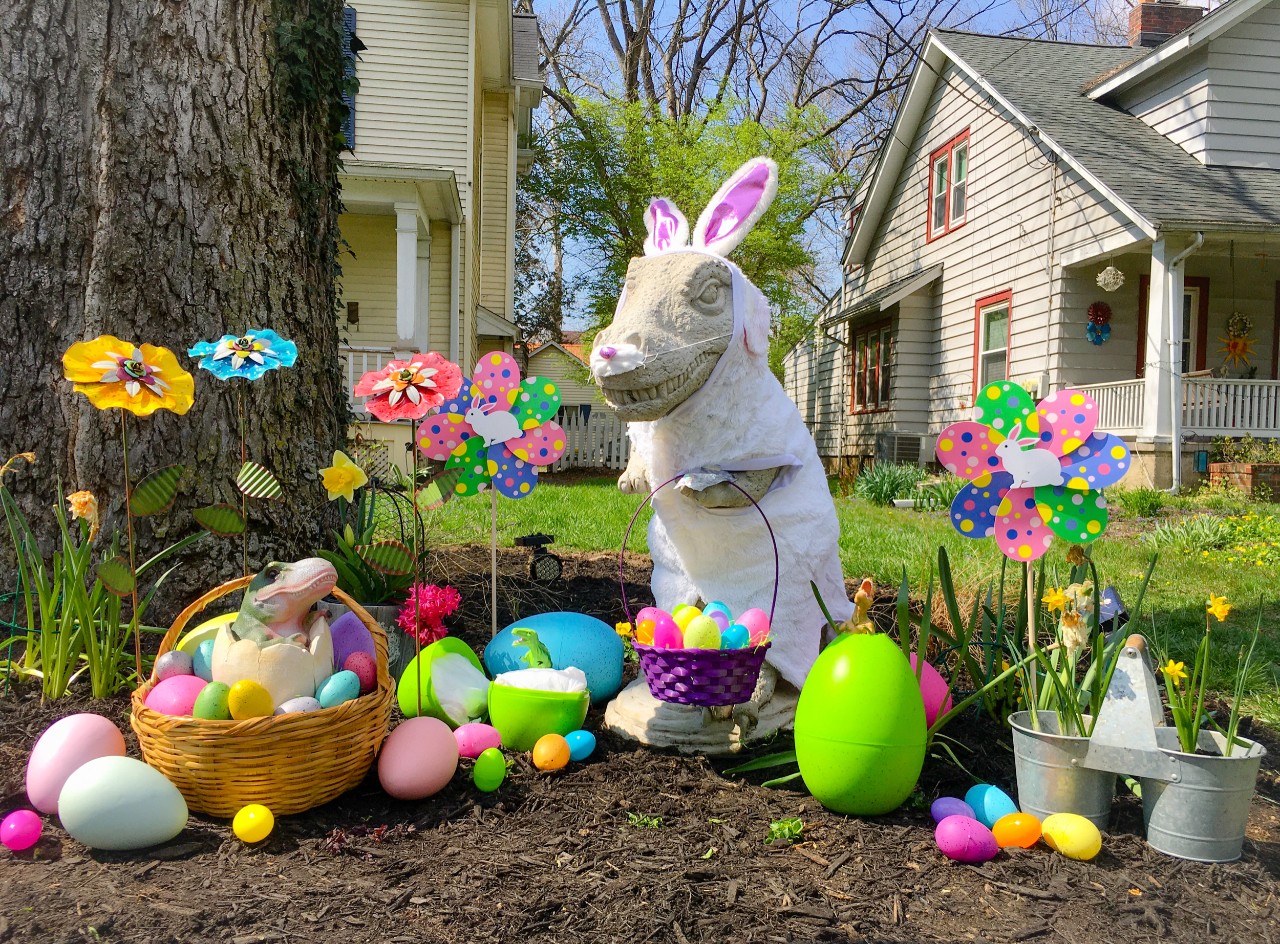 A cement T-Rex statue decorated as an Easter bunny surrounded by plastic eggs.