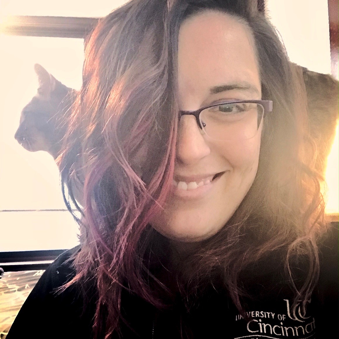 Girl wearing glasses with her cat standing on the back of her chair.