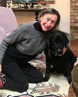 UC's Greer Glazer, dean of College of nursing, kneels with her black lab on a carpet.