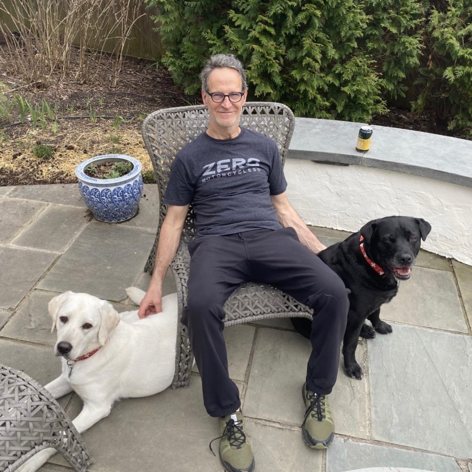 Man sits on patio with a black lab and a yellow lab dogs.