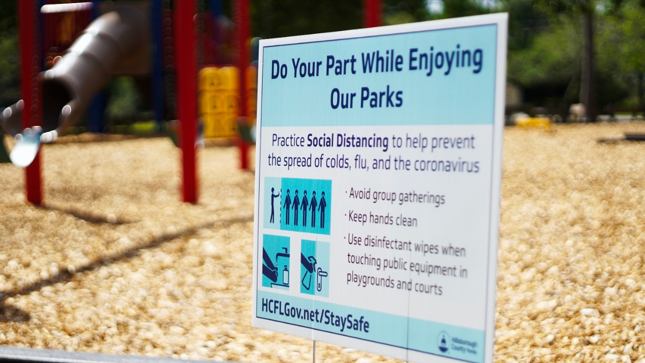 A sign at a closed playground reads: Do your part while enjoying our parks. Practice social distancing to help prevent the spread of colds, flu and coronavirus. 
