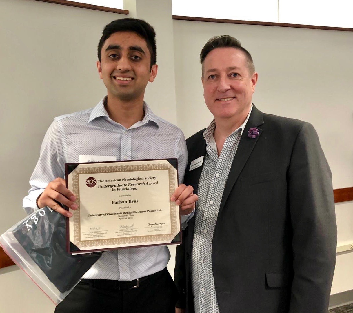 UC's Bryan Mackenzie and Farhan Ilyas stand together holding a certificate.