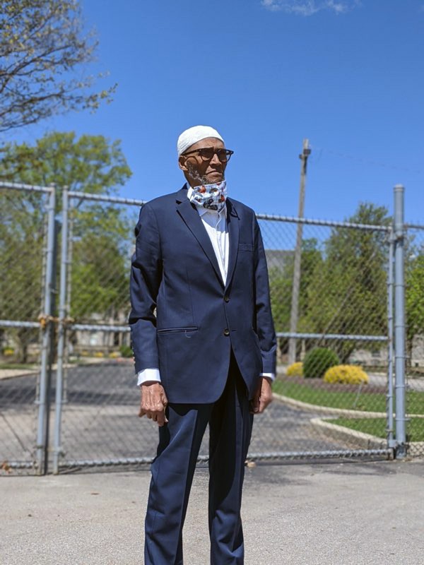 A man in a blue suit stands in front of a large metal gate