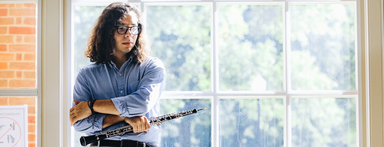 Leo De La Cruz stands with his oboe in front of a window