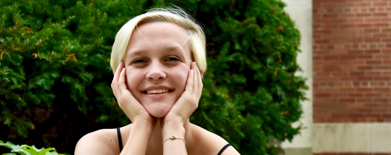 UC nursing grad Samantha Branham sits on lion statue in front of McMicken Hall.