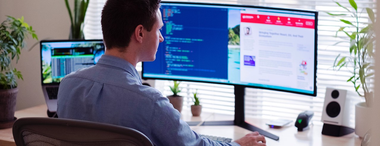 Business man working from home with laptop and widescreeen monitor.