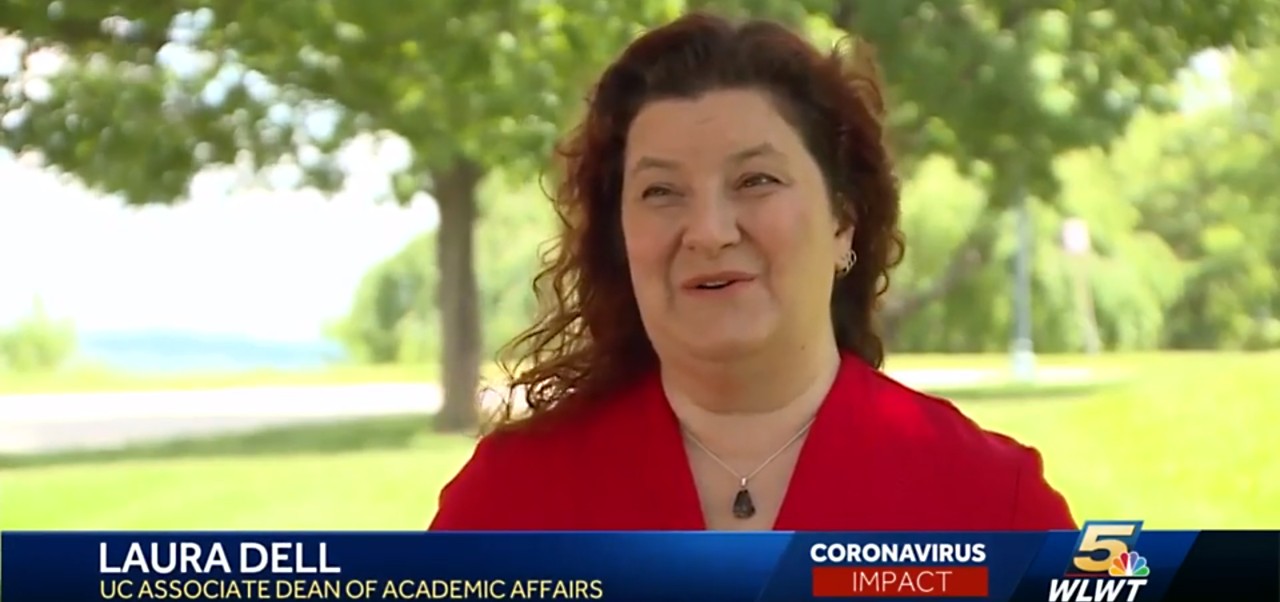a woman with dark curly hair wearing a red shirt talks to the media