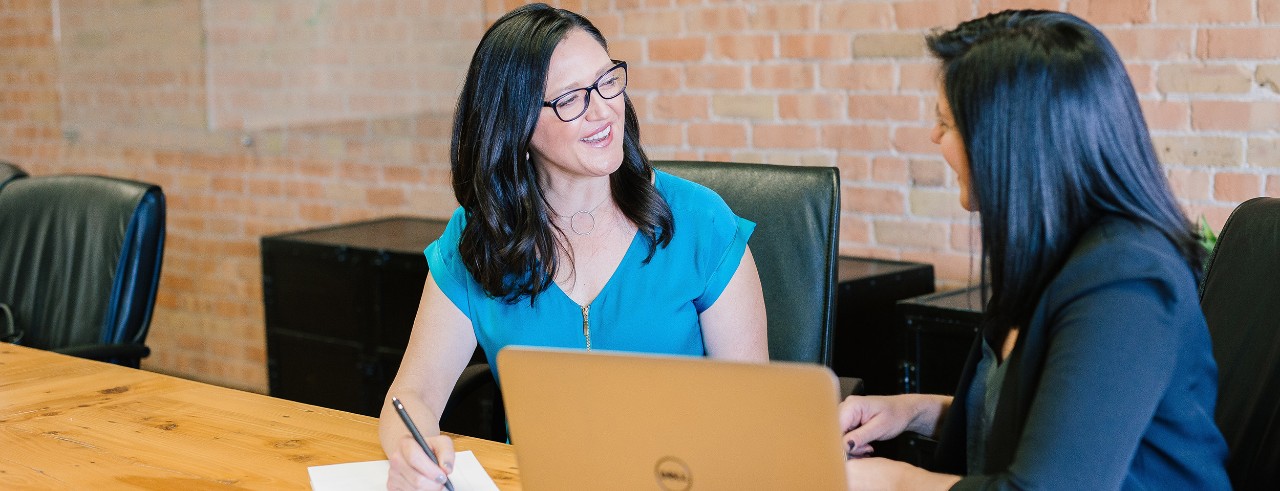 Two women talking in conference room about business deal.