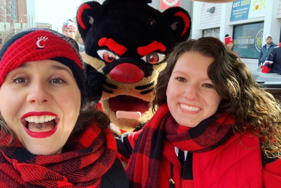Grace Hertlein, dressed warmly for a football game, poses with a friend and the UC Bearcat.