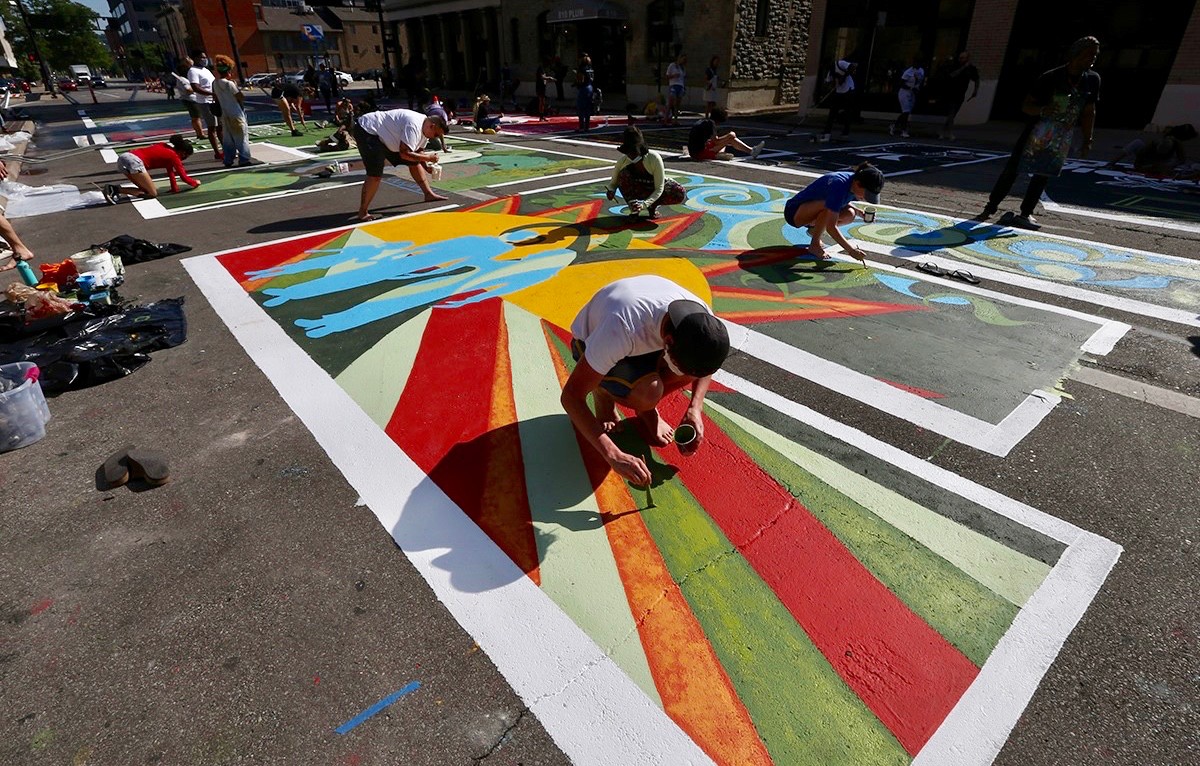 UC's Cedric Cox leans over painting his letter E design as part of Cincinnati's Black Lives Matter! street mural.