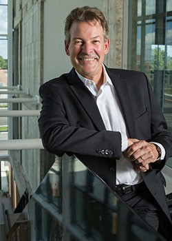 man in sports coat and buttondown shirt leaning against railing at top of a staircase