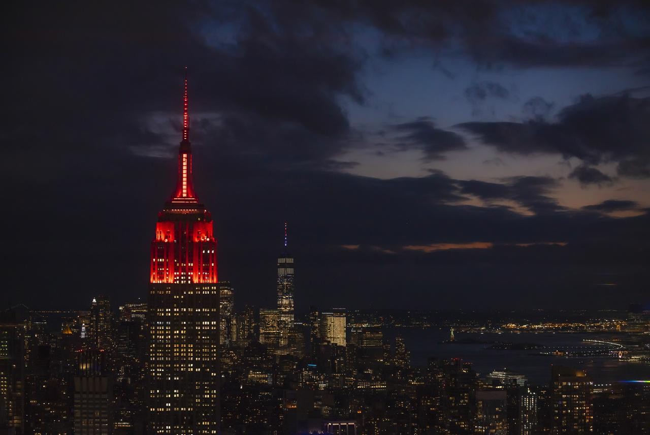 The Empire State Building is lighted in red against the New York backdrop.