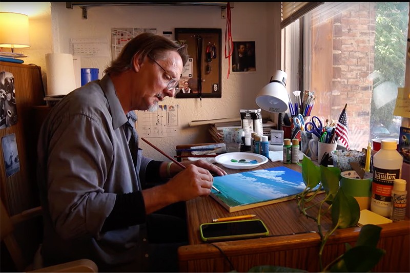 A man painting at his craft table