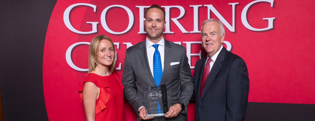 A business man receiving an award with a business woman and another business man on each side of him at an awards event.