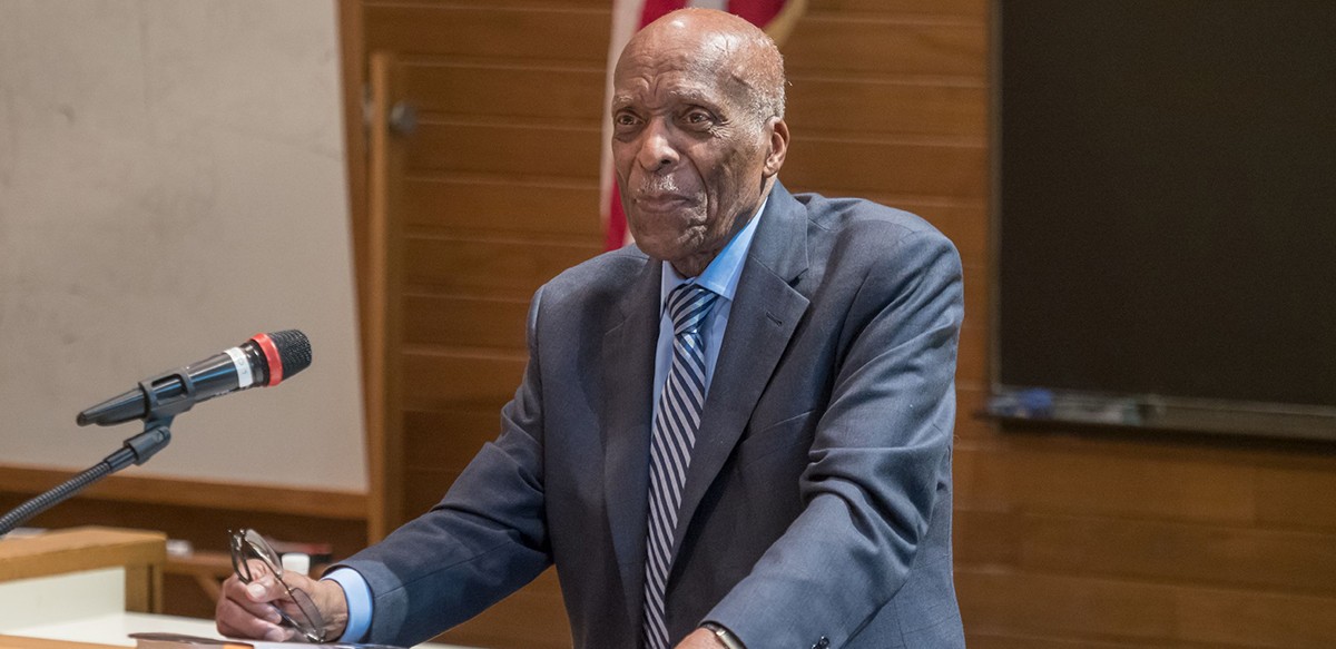 a man in a grey suit stands before a lecturn