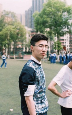 Zhang stands on a lawn with people and buildings in the distance