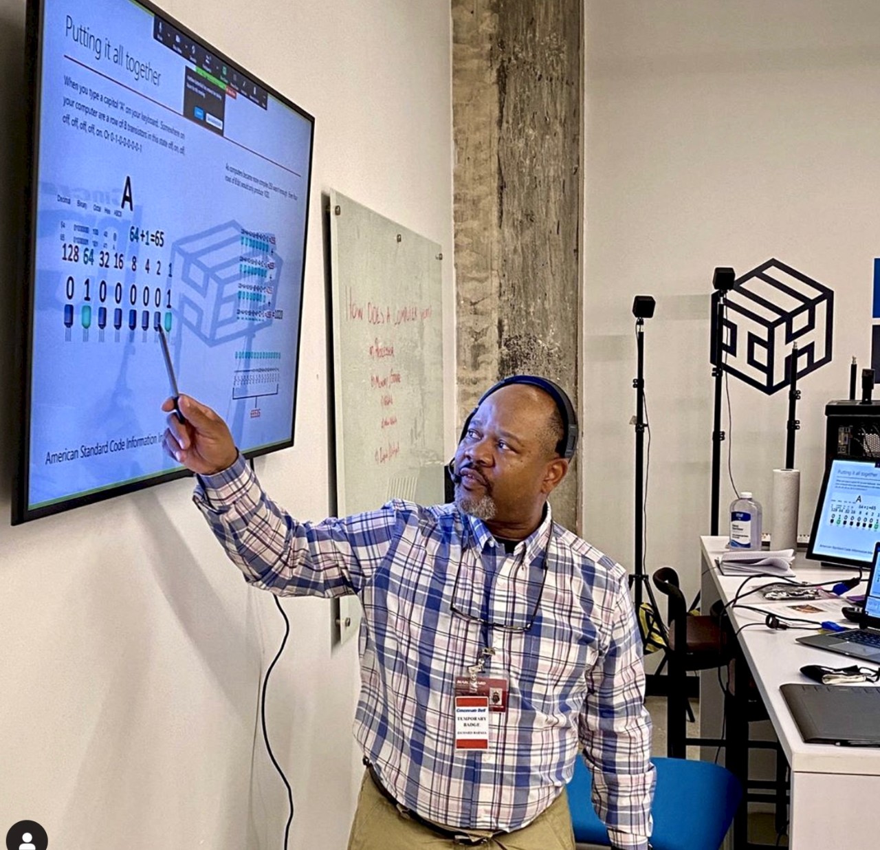 An instructor points to a white board on a wall as he teaches computer programming skills in UC's 1819 Innovation Hub.