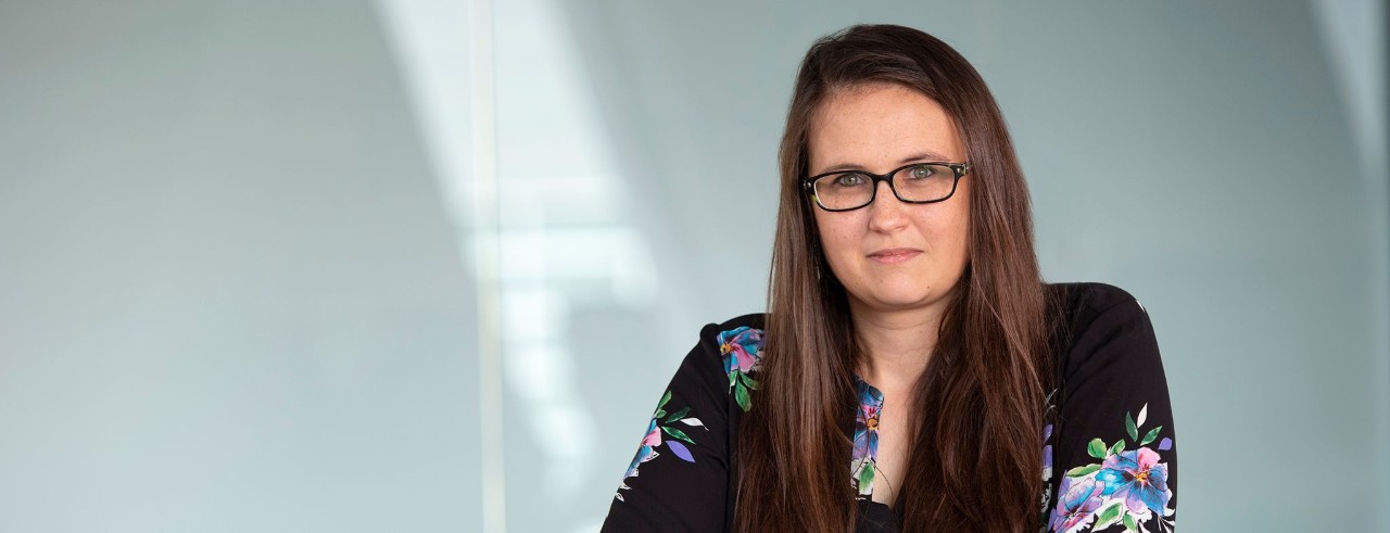 A woman wearing glasses with long brown hair and a colorful blouse 