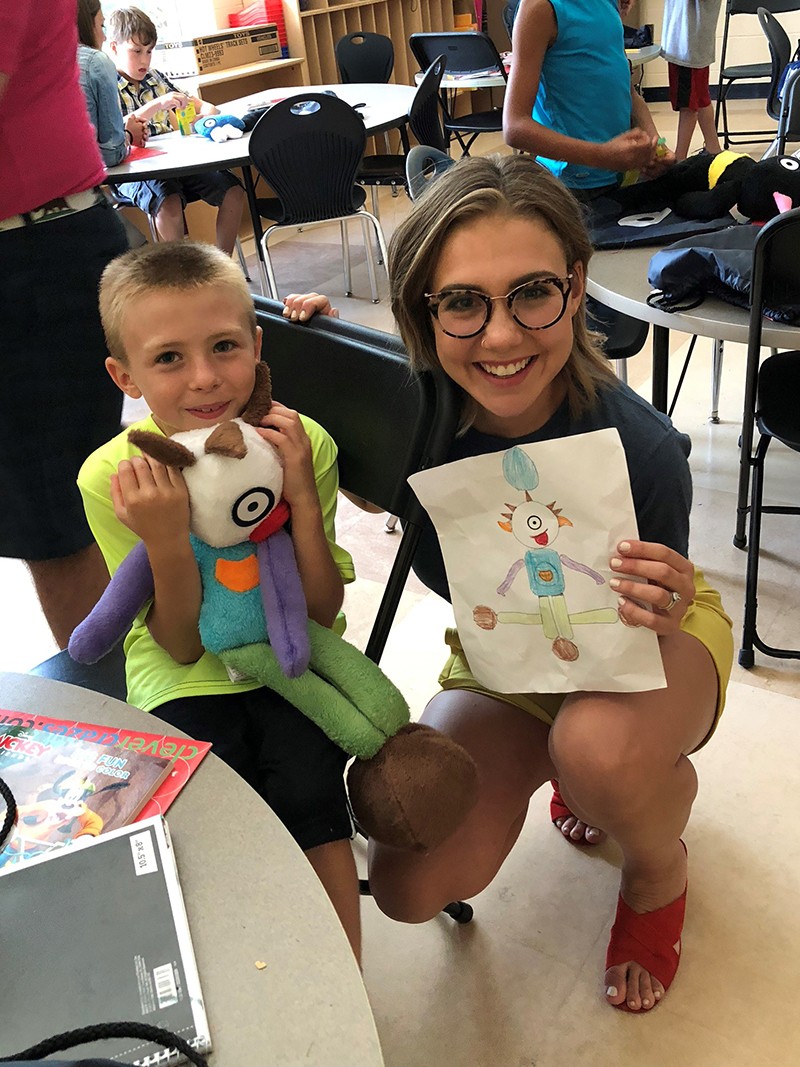 Macy poses with a student and their drawing