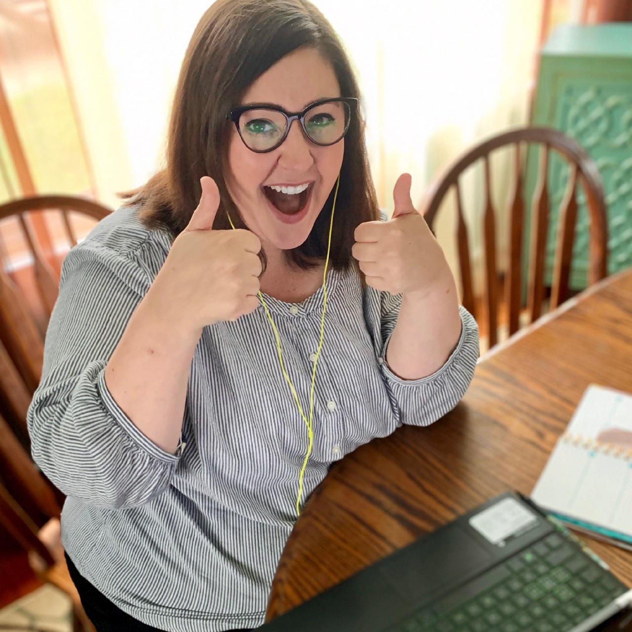 UC female student sits at a table with a laptop computer holding both thumbs up while smiling.
