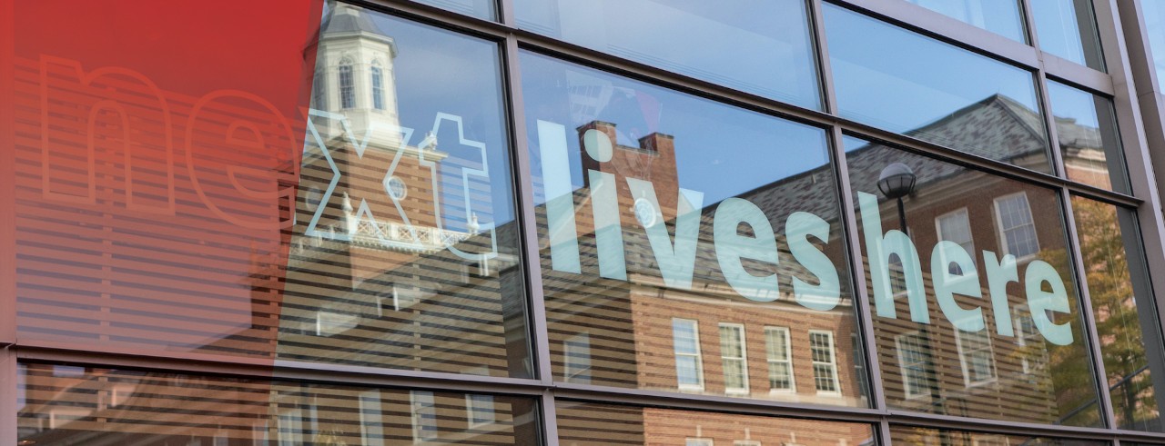 Reflection of a building that says Next Lives Here