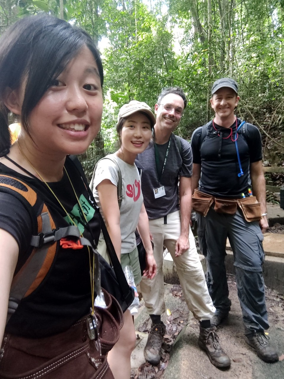 Four people wearing backpacks pose for a selfie in a rainforest.