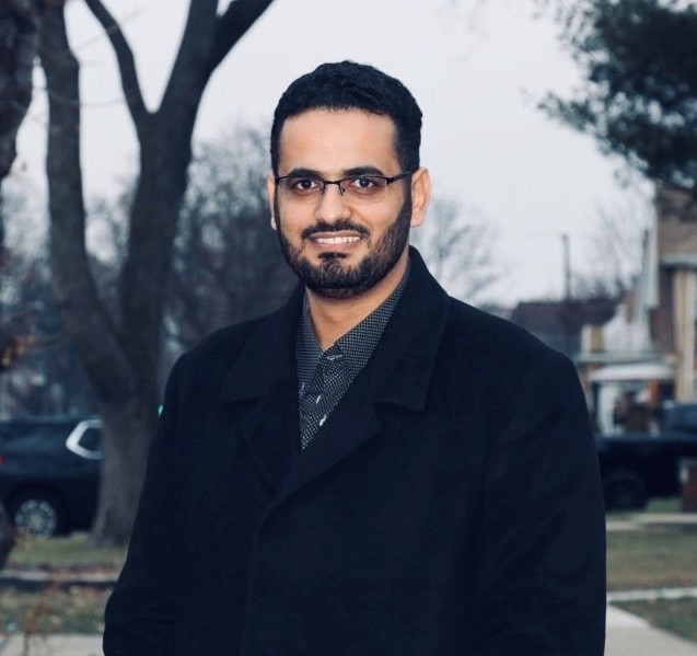A smiling man wearing glasses standing outside in a neighborhood.