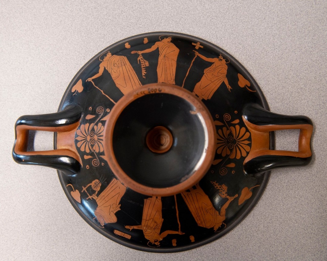 A cup features six male figures holding staffs or musical instruments on the underside of a wine cup.