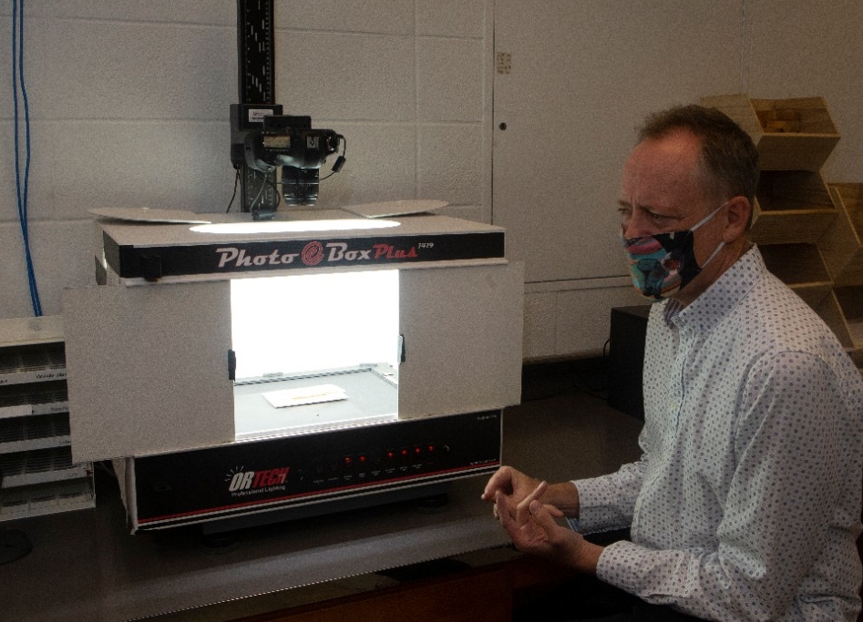 Eric Tepe sits at a lab bench in front of a lightbox with a camera mounted above it.