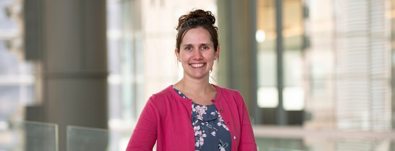 A woman smiles at the camera while standing on a pedestrian bridge in the CARE/Crawley Building at the UC College of Medicine