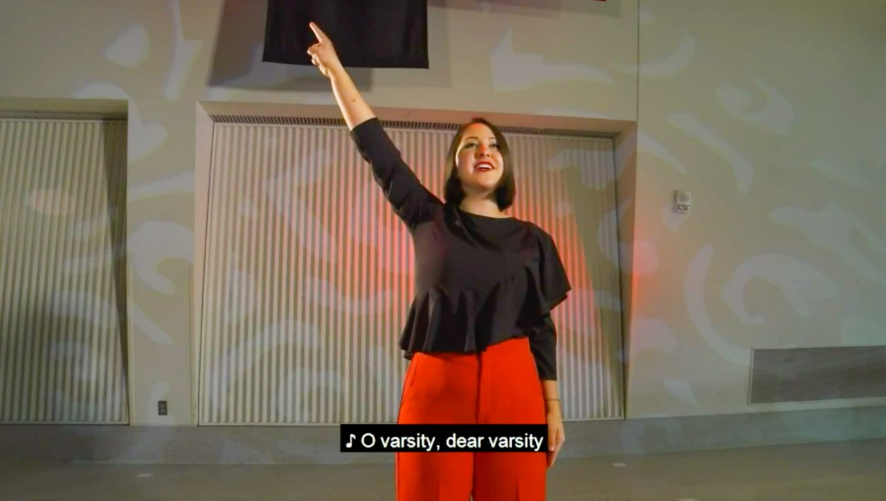 A UC student sings the alma mater in front of a projected decorative image.