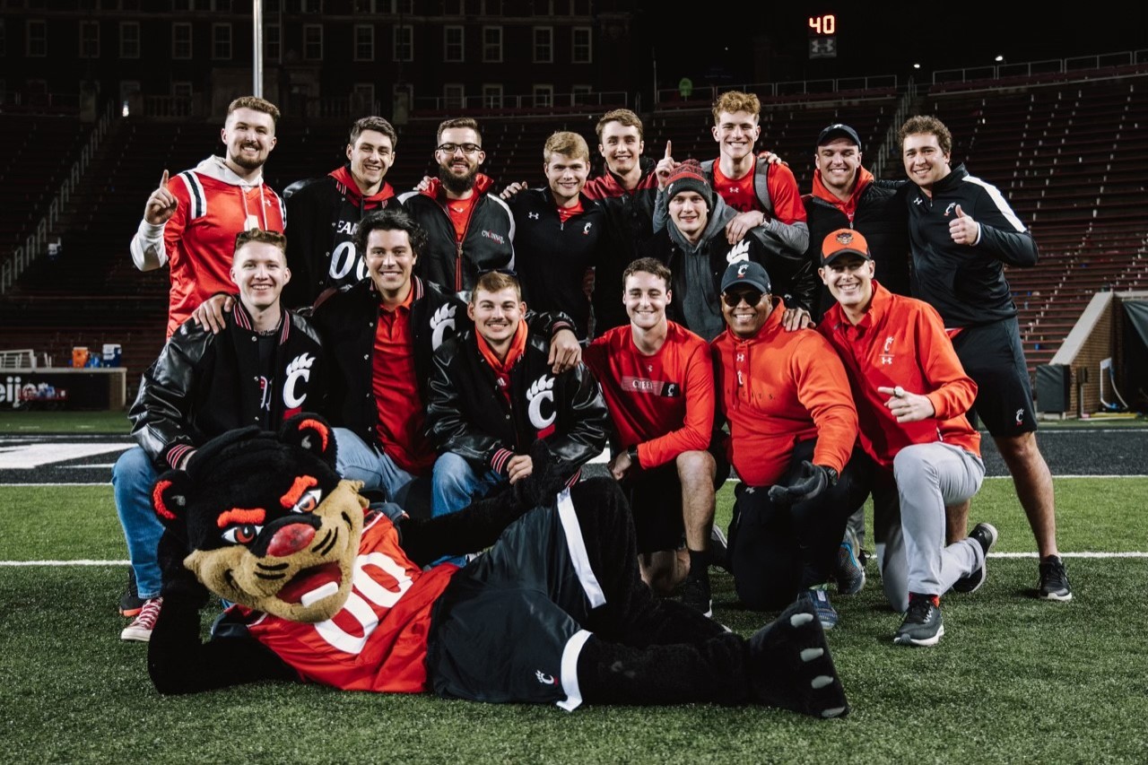 Bearcat mascot joins a group of UC fans for a photo on Nippert field. 