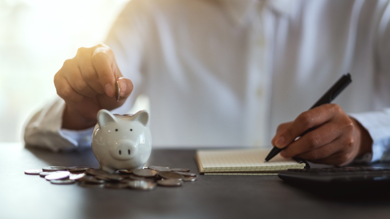 Closeup image of a woman putting coins in a piggy bank and taking note for saving money and financial concept