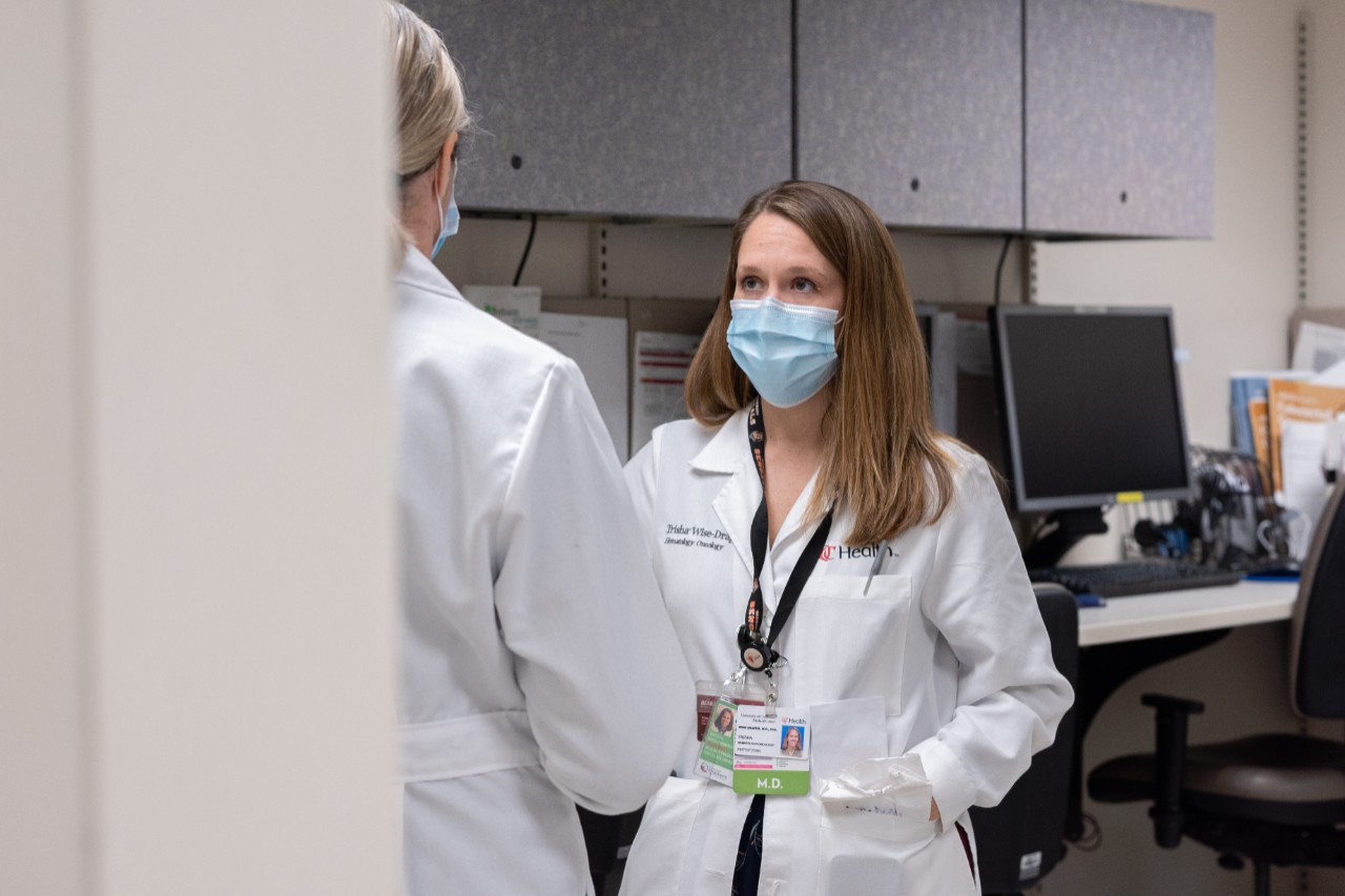 Dr. Wise-Draper wears a mask and stands talking with another health care worker